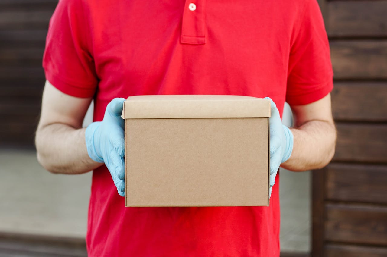 about-01 A delivery person in a red polo shirt and gloves holds a cardboard box, ready for delivery.